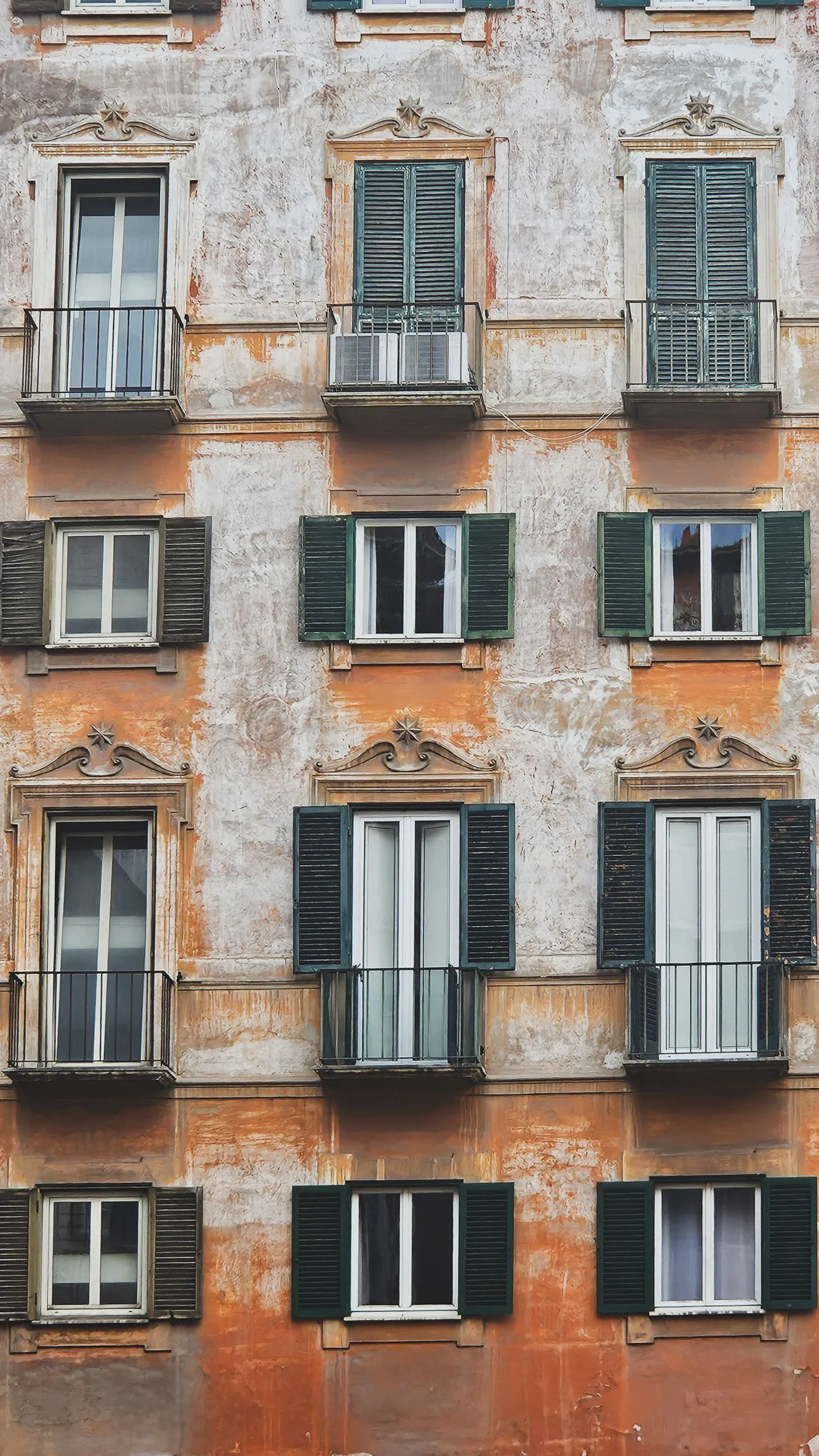 Facciata di un palazzo storico italiano con l'intonaco ammalorato, le persiane e i balconcini in ferro