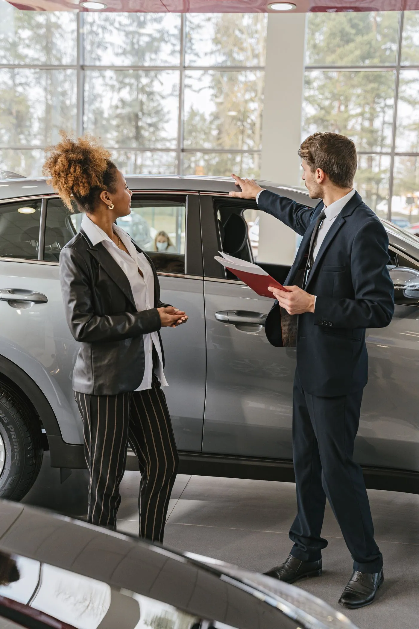 Una professionista e un consulente valutano un'auto aziendale nel salone di una concessionaria, documenti alla mano